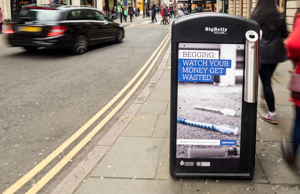 A poster in England with a picture of syringes and the text "Begging: Watch your money get wasted"
