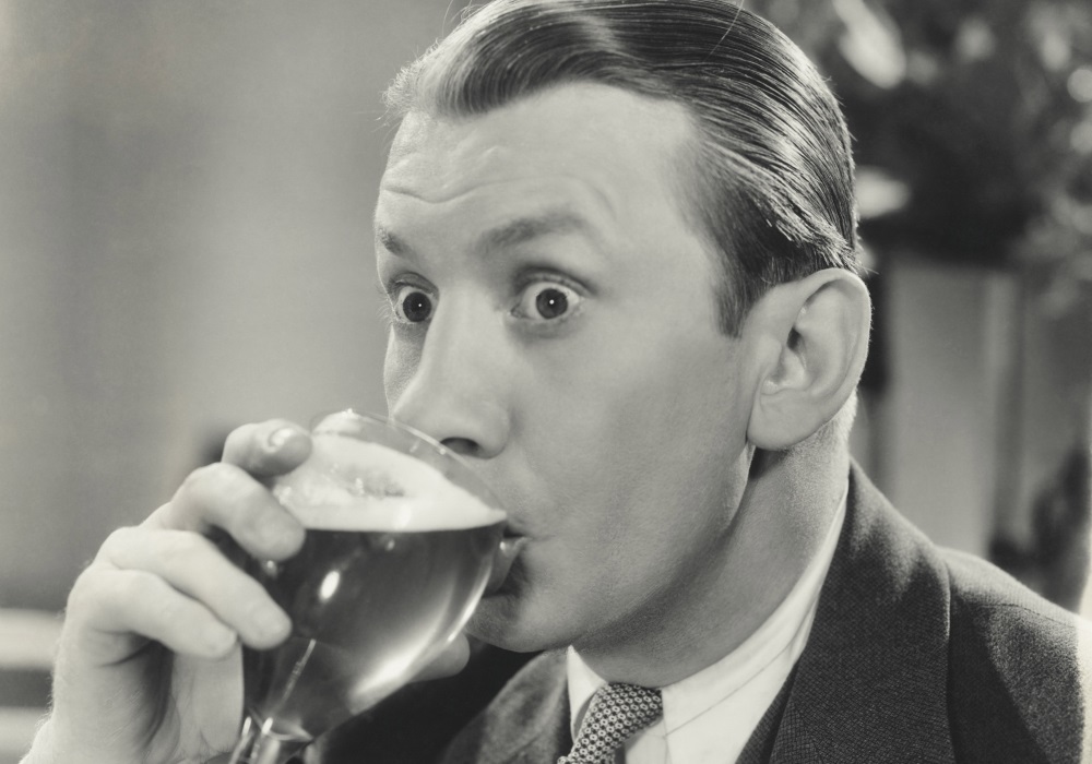 Black and white photo of a man drinking a foamy drink out of a glass.