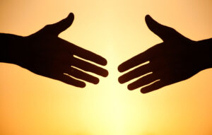 Hands reaching to touch each other in front of bright yellow light.