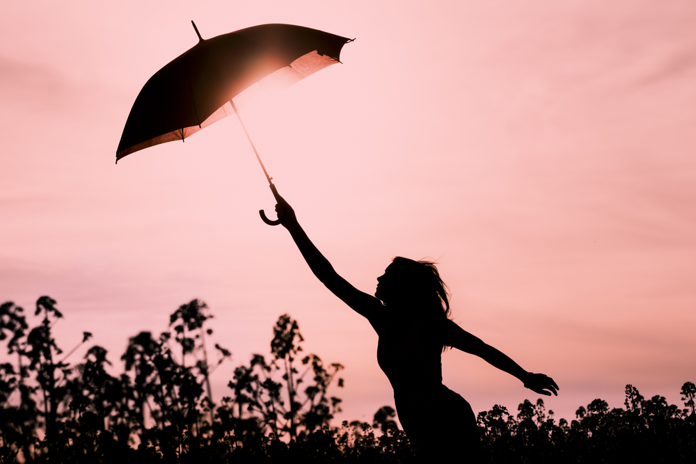 A silhouette of a woman holding an umbrella in front of a pink sky
