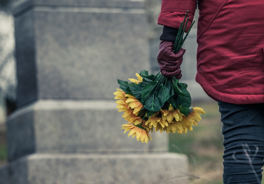 The back of someone holding flowers at a grave.