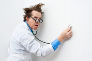 A doctor with wild hair holds his stethoscope against a wall.