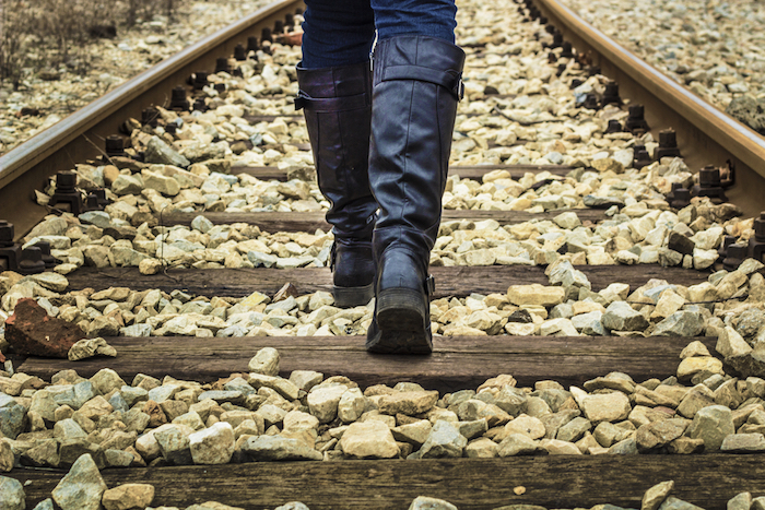 An image of someone walking on a train track, only showing the legs and feet.