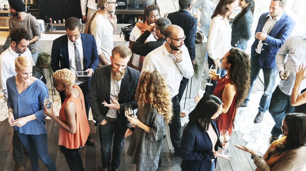 A shot from above of young people milling around in a big room, some holding drinks.