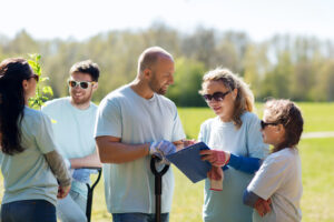 A group of people in matching teeshirts in a park, smiling, talking, and looking at a clipboard.