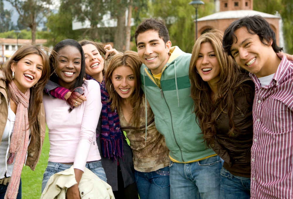 A group of young people smiling, arm in arm.