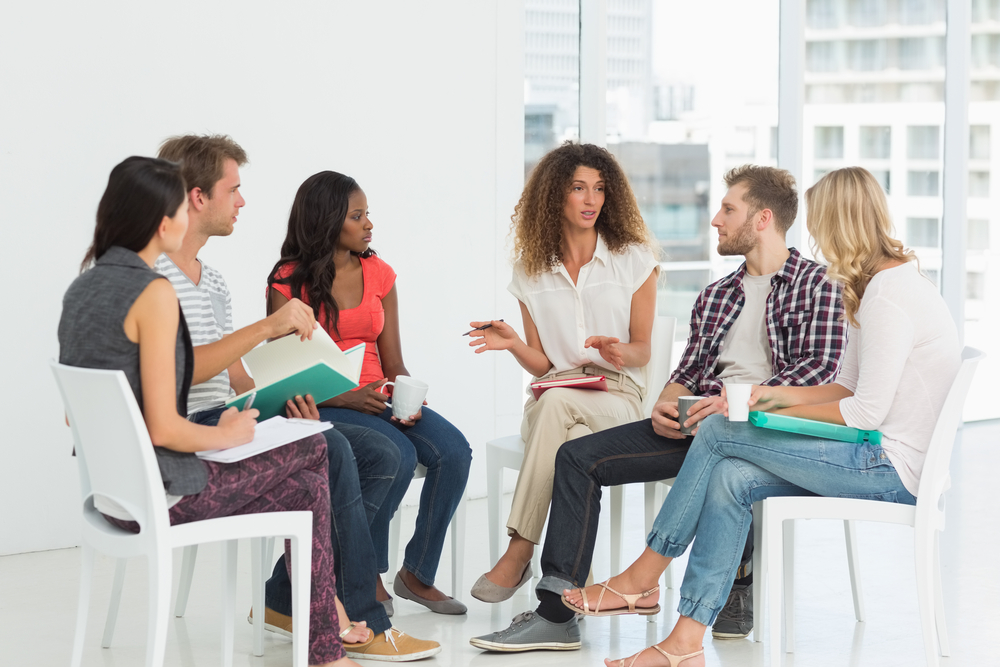 A group of people sitting in chairs, in therapy