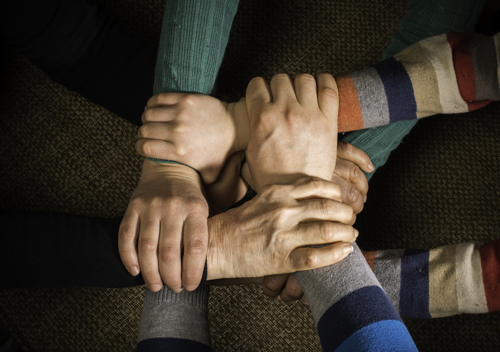 4 hands holding each other's wrists to form a square.