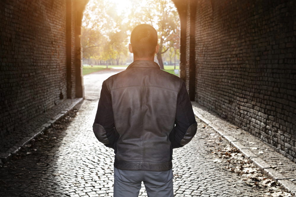The back of a man standing in a tunnel, facing the sunshine and way out.