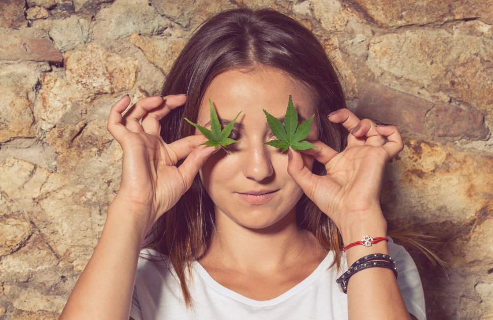 A woman holding marijuana leaves over her eyes.