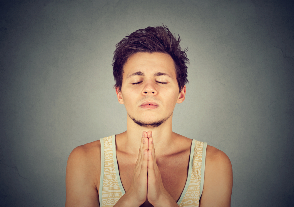 A young man holding hands together in prayer, eyes closed.