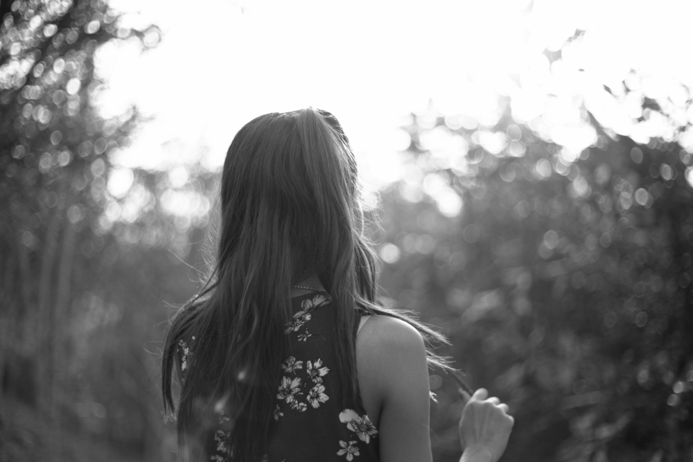 black and white image of back of woman with long hair, facing trees.