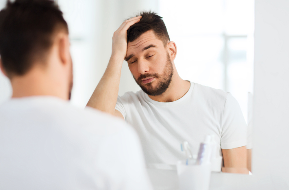 Man holding his head in front of a mirror.
