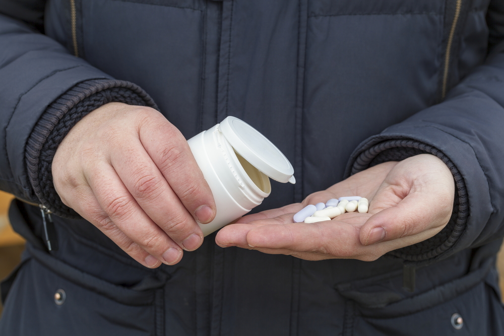 One hand holding a pill bottle pouring pills into other hand.
