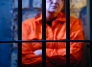 An inmate standing inside a jail cell with his arms crossed.