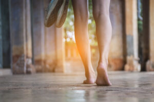Someone with bare feet holding shoes and walking forward.