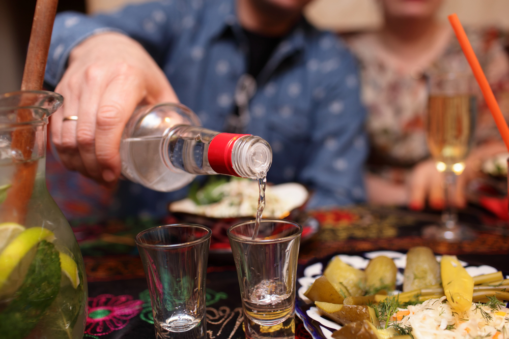 Person pouring vodka into shot glasses.