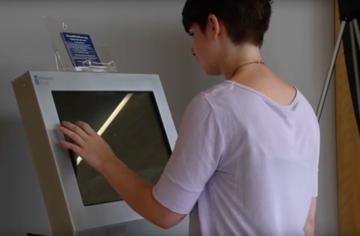 A student demonstrating how to use the mental health screening kiosk.