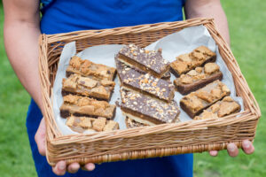 Person holding a wicker basket containing slices of homemade brownies with chocolate nuts and caramel.