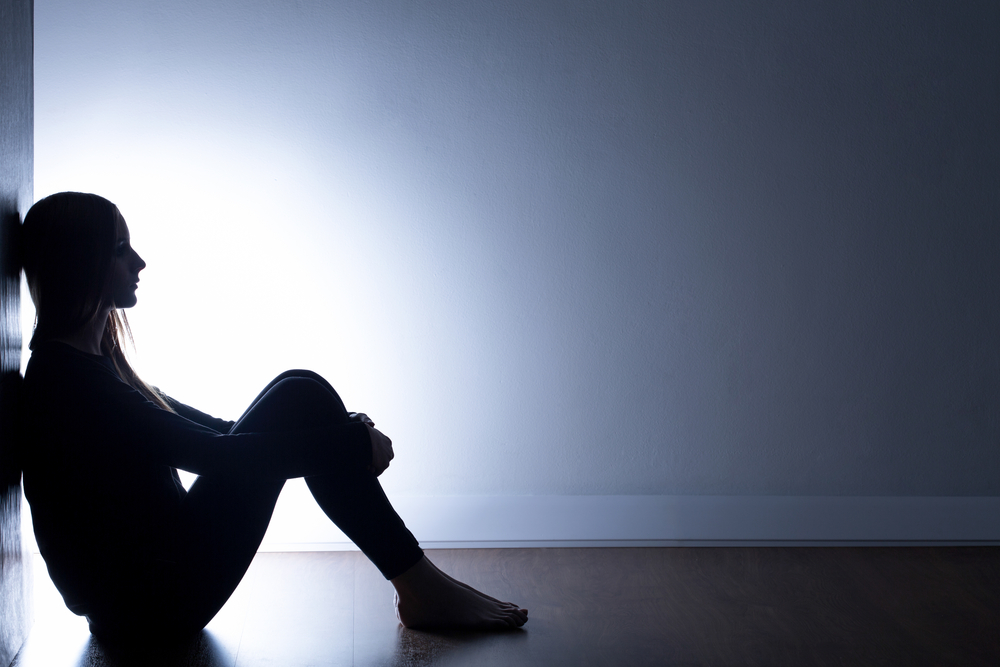 A person with depression sitting alone in a dark room.