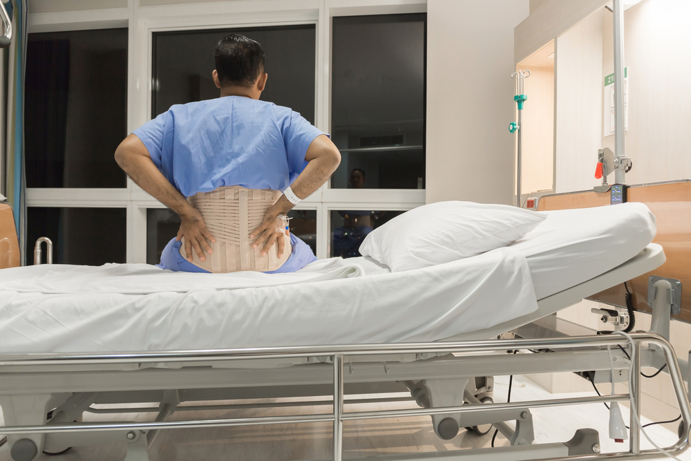 A post-operative male patient sitting on the bed in a hospital ward room.