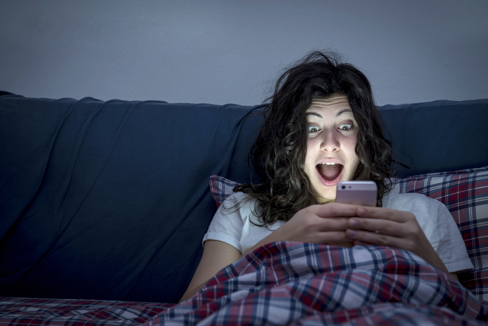 Woman losing sleep while checking her smartphone in bed.