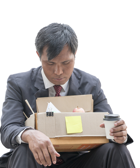A man sitting and looking depressed with a box of belongings and a cup of coffee.
