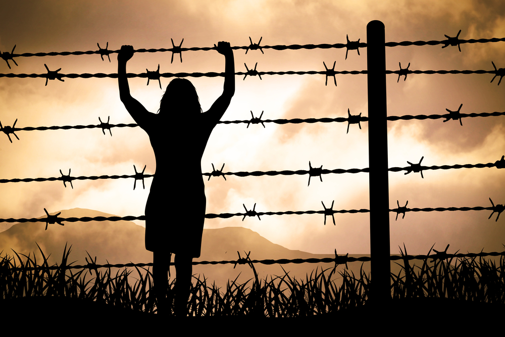 A silhouette of a woman behind barbed wire