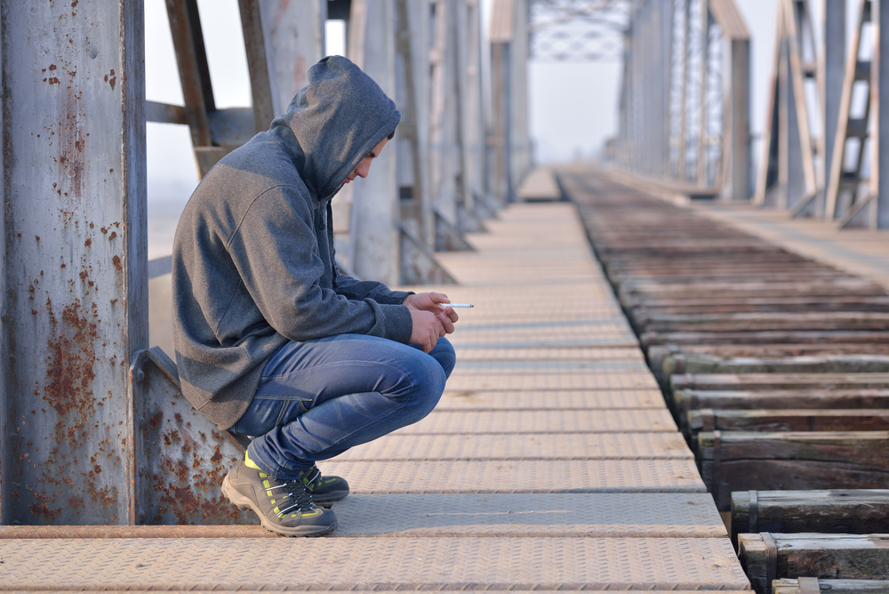 A man in hoodie crouching on a bridge, depressed.