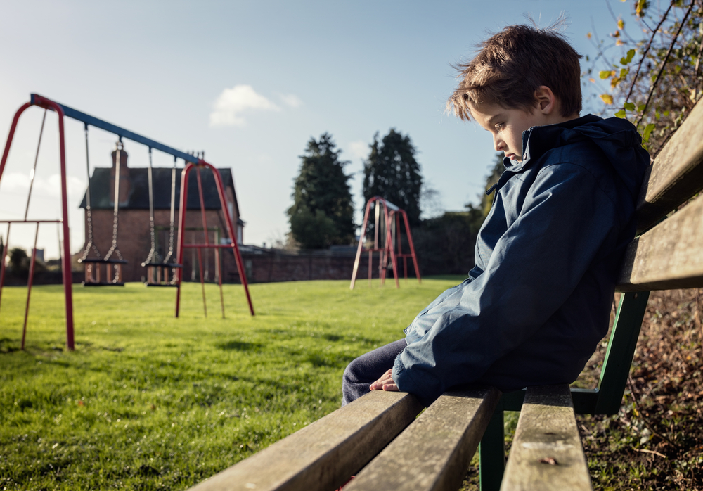 pensive kid sitting on a bench near an empty playground.