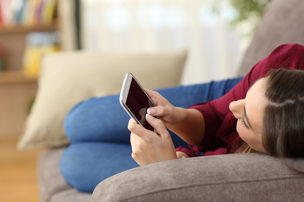 Teen laying on couch and using her smartphone.