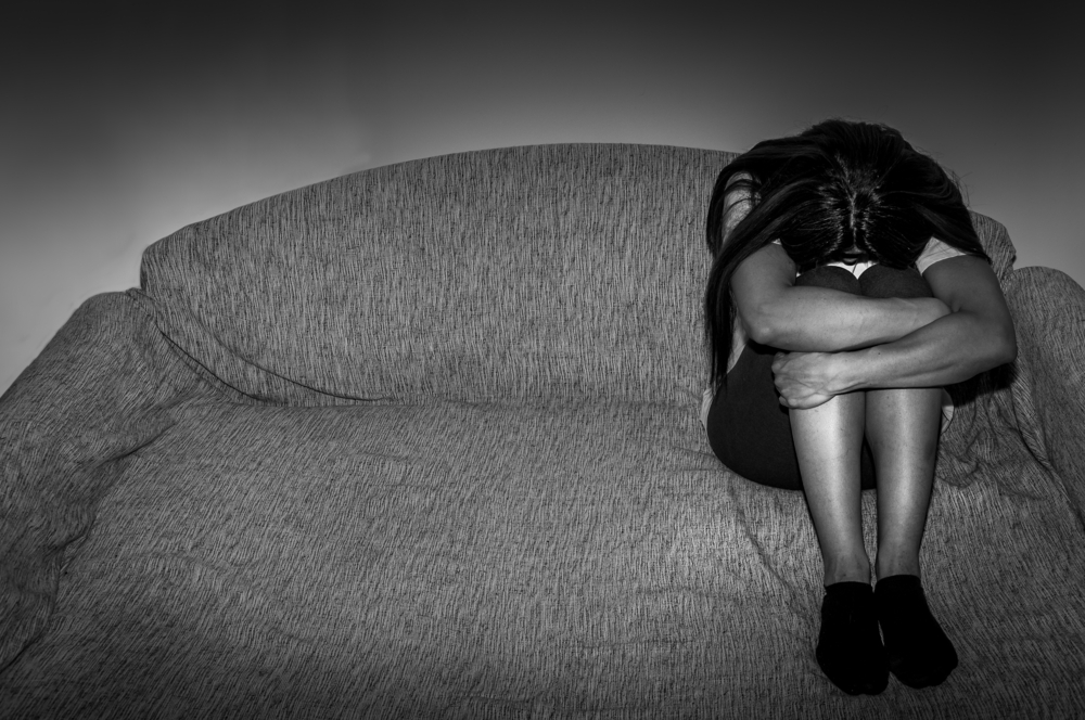 Sad grieving woman on couch arms folded over knees