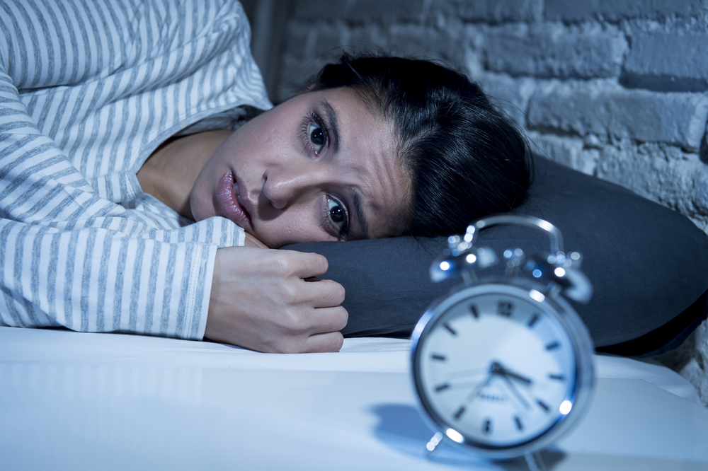 sleepless woman lying in bed staring at clock.