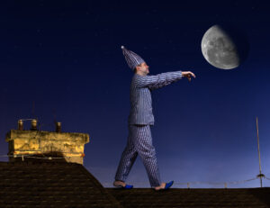 Somnambulist sleepwalker in pajamas and a night cap with hands forward walking on the roof on a background of the night sky with the moon.