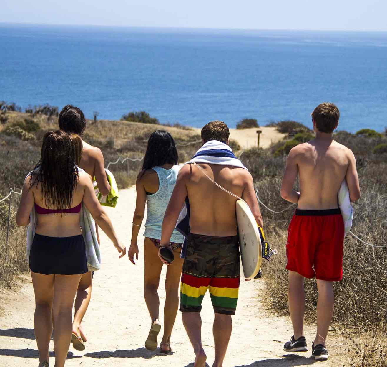 Young people walking to the beach, seen from the back.