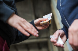 Two men exchanging cash for a baggie filled with a white powder substance