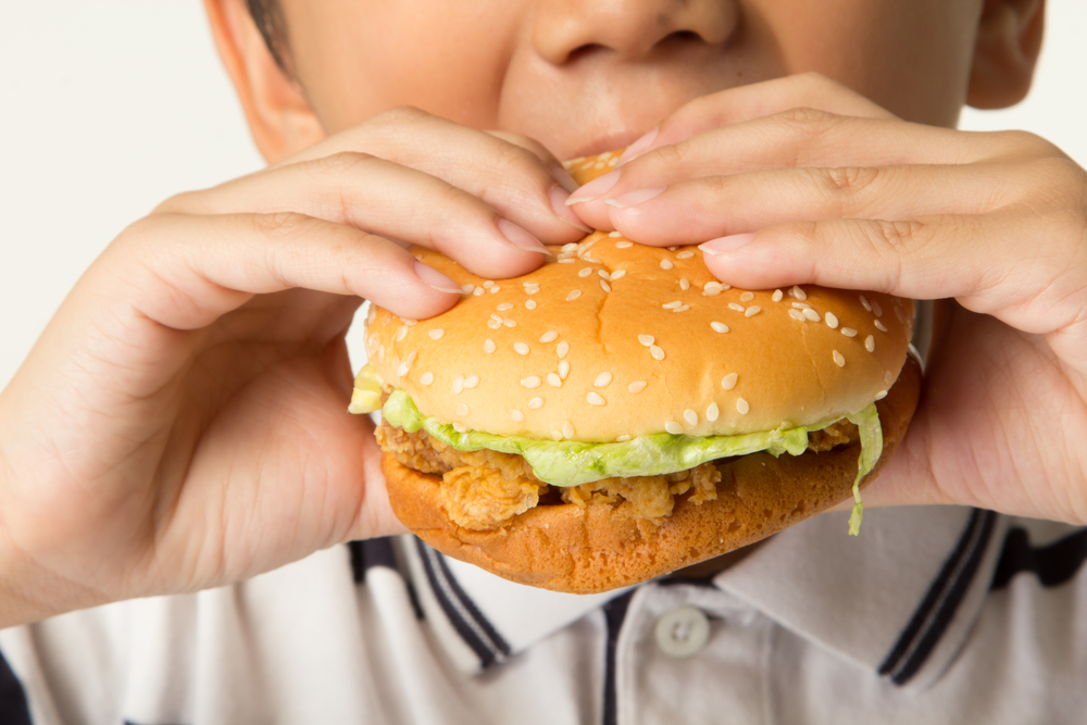 a young boy biting into a chicken sandwich.