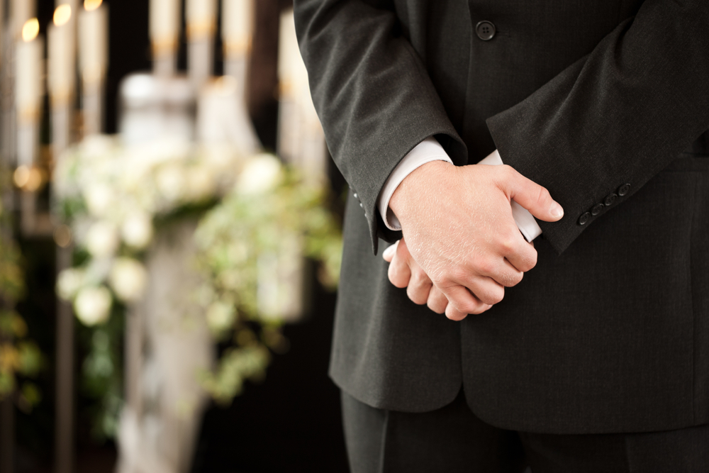 funeral director standing in front of urn and candelabra.