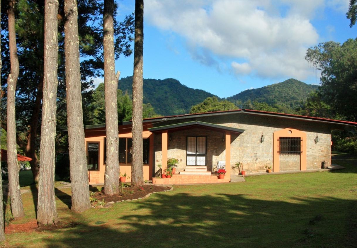 Serenity Vista, a single story building with green grass, palm trees, and mountains in the background.