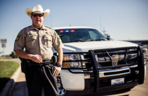 a texas police man standing near his car.