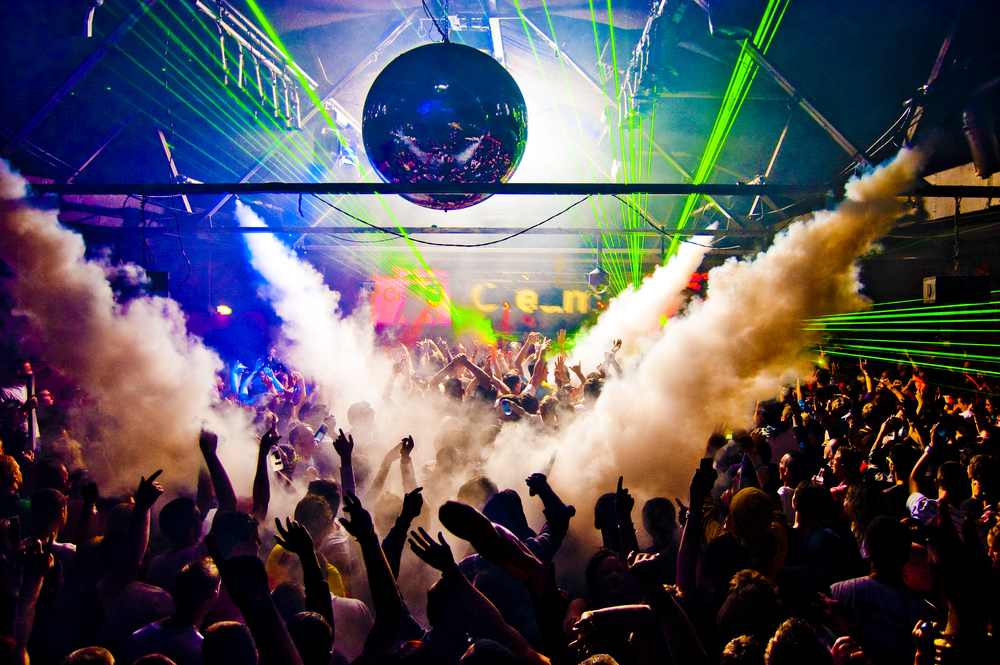 a crowd of ravers dancing inside of a smoke-filled venue