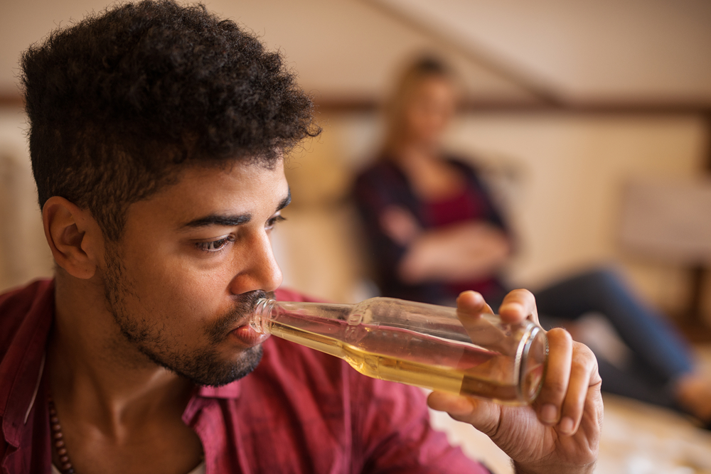 upset man drinking with girlfriend in background