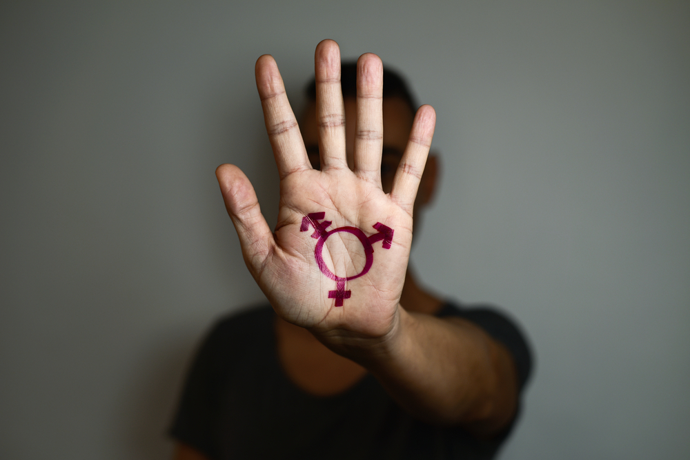 A transgender person holding up hand with trans sign