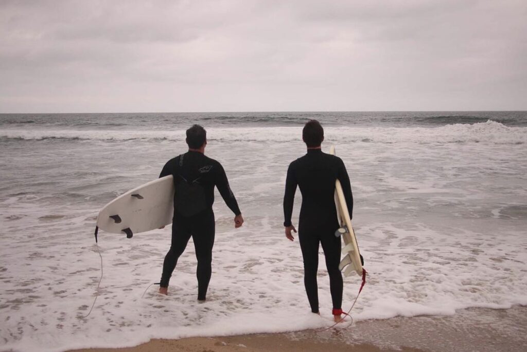 Two men standing at the beach holding surfboards, about to walk into the water