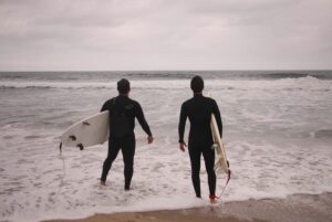 Two men standing at the beach holding surfboards, about to walk into the water