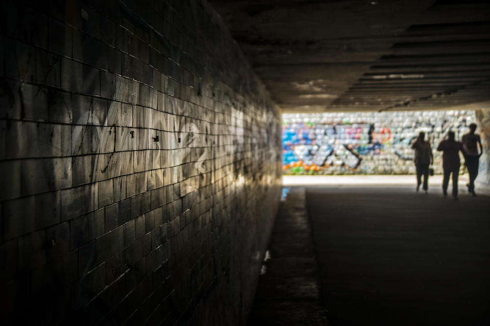 3 people walking through graffiti-covered underground tunnel