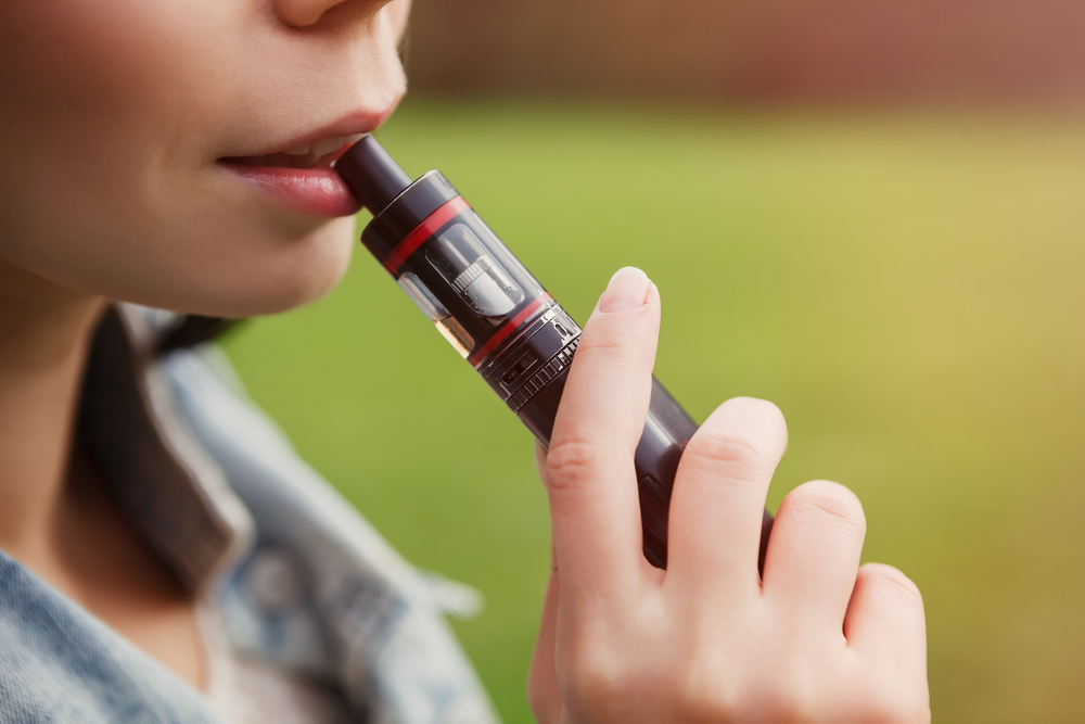 teen holding modern e-cig device mouthpiece in mouth