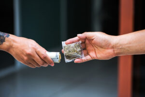 hands exchanging a baggie of marijuana for cash