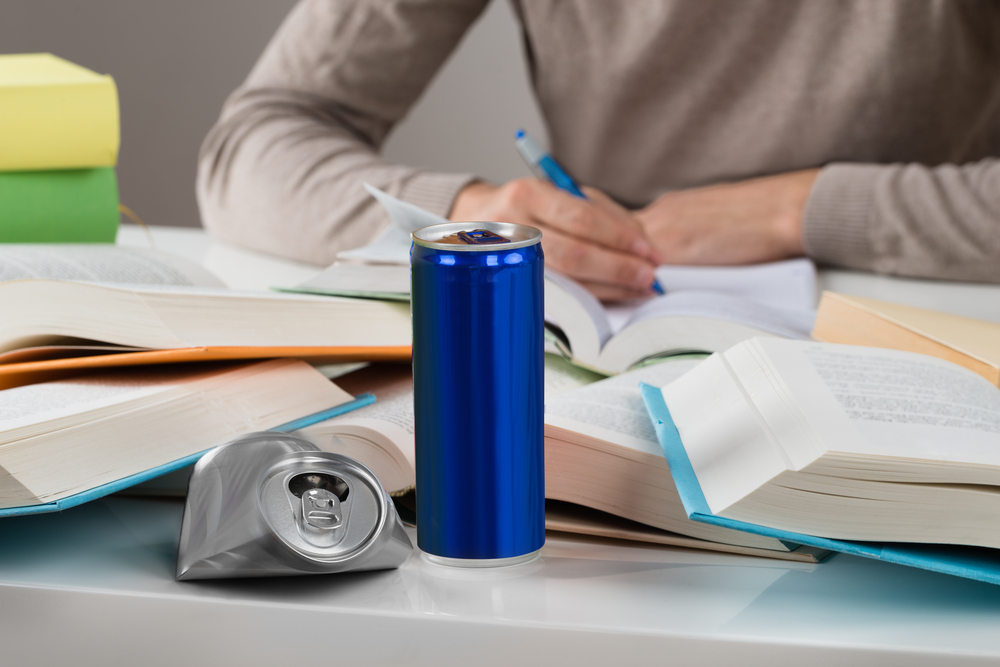 male student studying with crashed drink can and books at table