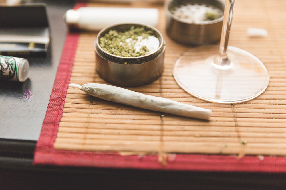 A joint of marijuana and a grinder alongside a wine glass.
